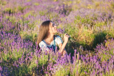 Genç güzel kız ellerinde çiçek bir buket ile bir lavanta çayır üzerinde oturur