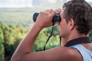 Genç bir adam dürbünle mesafeye bakıyor..