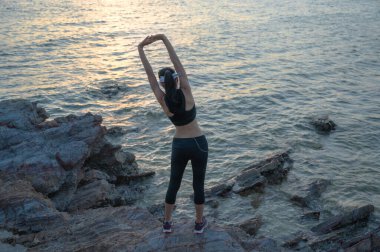 Kadın egzersiz öncesi hareketlerinde koşmadan önce deniz kıyısındaki kaya taşında ısınır.