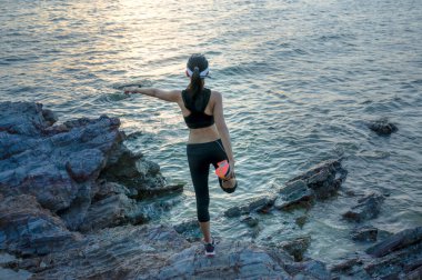 Kadın egzersiz öncesi hareketlerinde koşmadan önce deniz kıyısındaki kaya taşında ısınır.