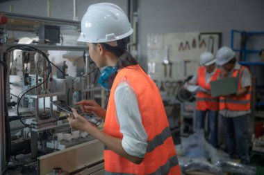 Mühendislik ya da teknik denetim yapan kadın kontrol listesi bölümü ve kalite kontrolü, takım çalışması ile birlikte iş yeri ve denetim sisteminde çalışılmasını sağlamak için makine sistemini kontrol eder.