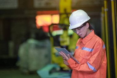 Kadın Mühendislik Mühendisi akıllı fabrikada yeni olan robotik markaların sistemini inceliyor ya da test ediyor. Robotik makineler, insan kontrolüyle birlikte çalışıyor.