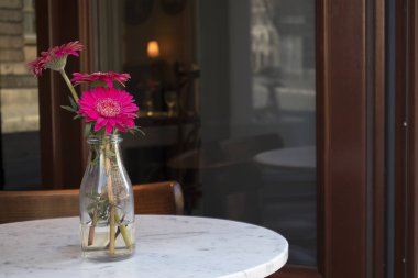 Bir bardak kırmızı gerbera dar sokak bir kafede bir masada vazo