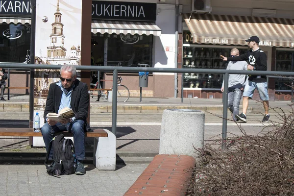 Starszy człowiek czyta gazetę siedząc na ławce w pobliżu rynku — Zdjęcie stockowe