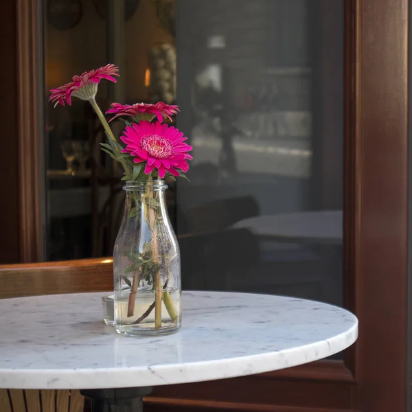 Bir bardak kırmızı gerbera dar sokak bir kafede bir masada vazo — Stok fotoğraf