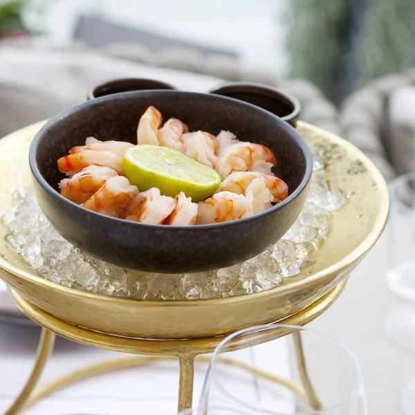 The Shrimps with lime in a cast-iron bowl in the ice on a table in a restaurant — Stock Photo, Image