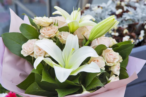Białe lilie i kolorowe róże w papier pakowy, jako prezent urodzinowy — Zdjęcie stockowe
