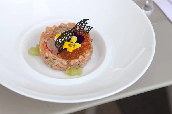 The Tartar from salmon with red caviar decorated with violet flowers and caramelized decoration — Stock Photo, Image