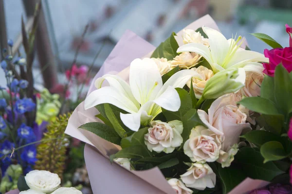 Białe lilie i kolorowe róże w papier pakowy, jako prezent urodzinowy — Zdjęcie stockowe