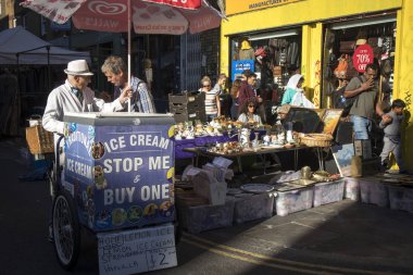 Londra, İngiltere - 14 Eylül 2018: Bricklane Doğu Londra'da sokakta insanlar. Dondurma bisikletle şapkalı yaşlı satıcı Bricklane üzerinde sürmek