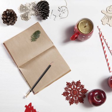 Elleri kalem defter tarafından çizmek bir kadınlar. Masada bir fincan çay limon, kar tanesi, Noel oyuncaklar ve elma ile var