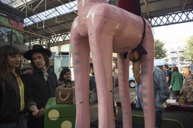 Londra, İngiltere - 15 Eylül 2018 Tower Hamlets eski Spitalfields pazarda kaplı. Bir erkek ve bir kadın bir oyuncak pembe zürafa ahşap genital muayene.