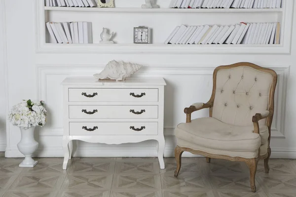 Interior of hite roomwith bookshelves, an armchair and a chest of drawers.