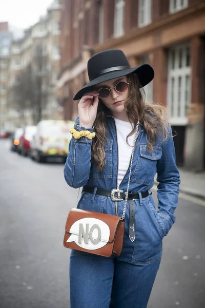 Bir kız bir mavi kot tulum ve geniş ekledi şapka yolun ortasında duruyor — Stok fotoğraf