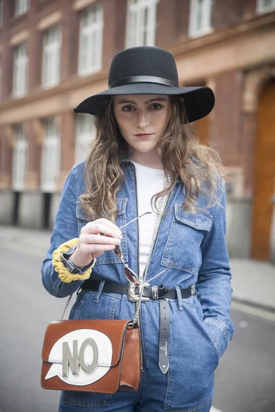 Una ragazza in tuta blu denim e cappello a tesa larga si trova in mezzo alla strada — Foto Stock