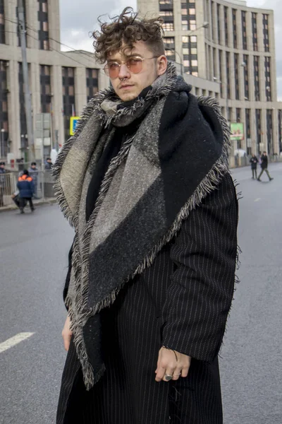 Σγουρά νεαρός άνδρας ντυμένος με ένα μακρύ μαύρο παλτό ριγέ και καρό μαντίλι και γυαλιά ηλίου ροζ — Φωτογραφία Αρχείου