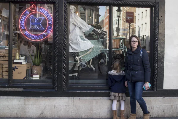 Mãe e filha perto da vitrine Liberty. Na janela do esqueleto em um manto branco andando de bicicleta — Fotografia de Stock