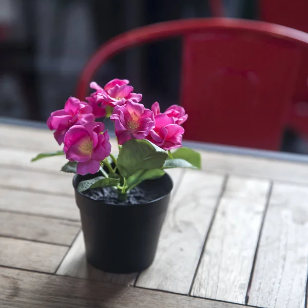 Las rosas rojas artificiales en el puchero adornan la mesa en la cafetería de la calle — Foto de Stock