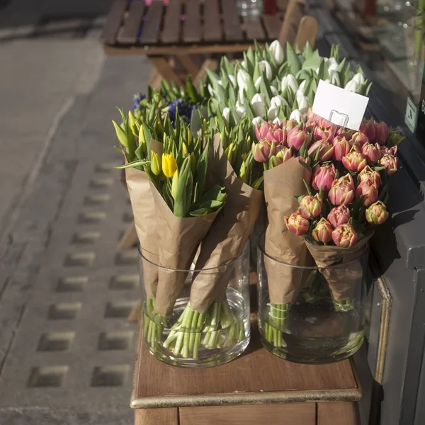 The Bouquets of multicolored tulips in Kraft beige paper in transparent vases for sale at the entrance to the store — Stock Photo, Image