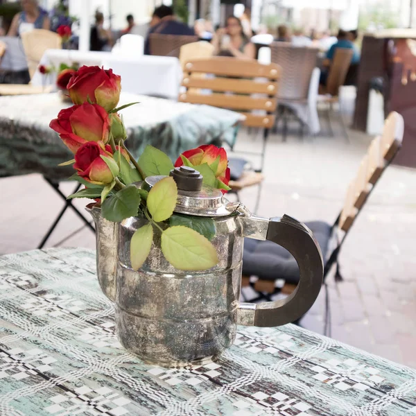维尔纽斯老城，红玫瑰在一个银色咖啡壶在街头咖啡馆的桌子上装饰 — 图库照片
