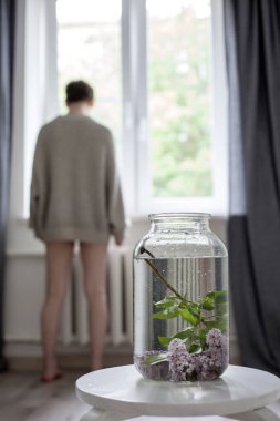 iç bir dekorasyon olarak beyaz sandalyeüzerinde şeffaf yeşil bir kavanozda leylak dalları buket