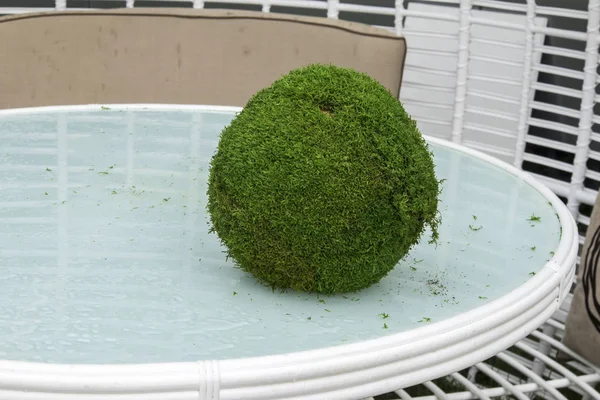 Uma bola de grama artificial encontra-se em uma mesa de vidro como uma decoração de jardim . — Fotografia de Stock