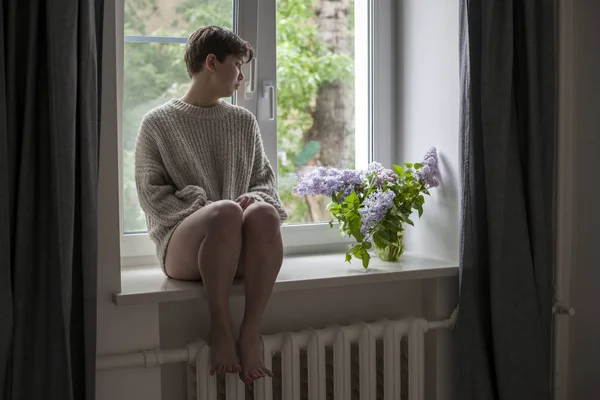 Het boeket van lila twijgen in een transparante pot op witte stoel als decoratie van interieur. Het meisje zit op het raam — Stockfoto