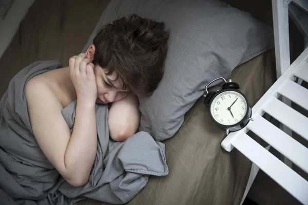 Ragazza, avvolta in una coperta grigia, stende la mano per spegnere l'allarme. Ci sono sei ore sulla sveglia. . — Foto Stock