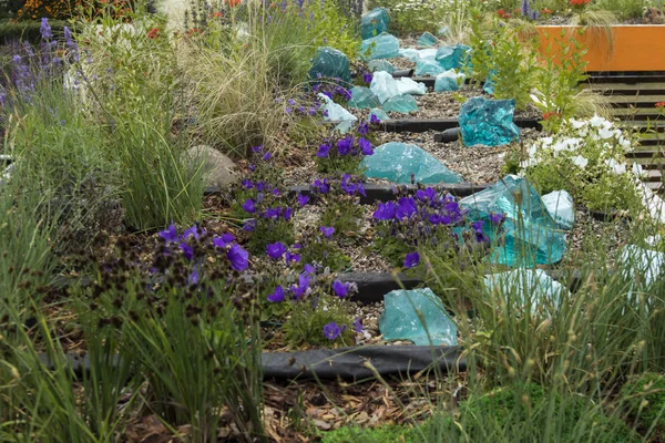 Trädgården dekoration med konstgjord sten gjord av grönt genomskinligt glas bland blommor — Stockfoto