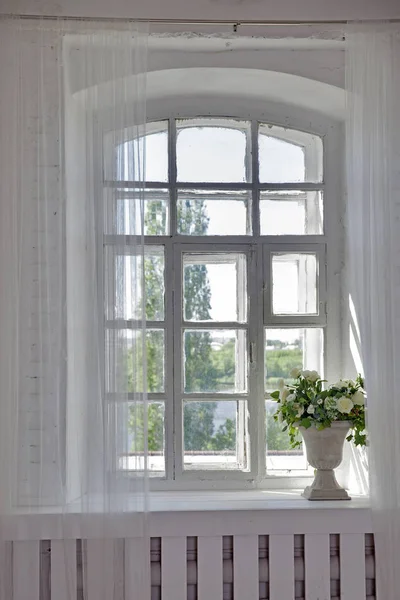 Strauß weißer Kunstrosen, Eukalyptus und Efeu in einer Steinvase auf der Fensterbank neben dem Fenster — Stockfoto