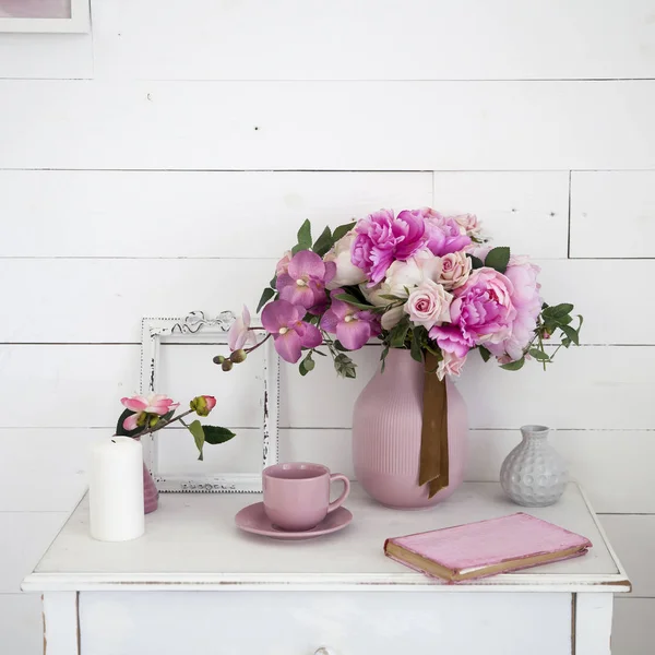 Boeket van orchideeën, pioenrozen, rozen in een keramieken vaas op het nachtkastje en een stapel boeken — Stockfoto