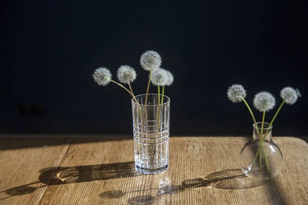 Löwenzahnstrauß in einem transparenten Glas auf dem Holztisch vor schwarzem Hintergrund — Stockfoto