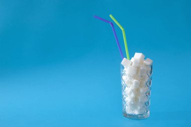 Pastel mavi arka planda şeker küpleri dolu saman ile şeffaf cam. Sağlıksız gıda konsepti.