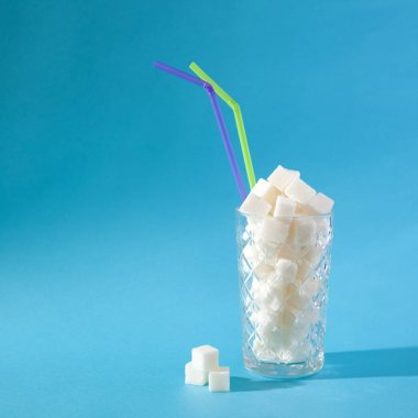 Pastel mavi arka planda şeker küpleri dolu saman ile şeffaf cam. Sağlıksız gıda konsepti.