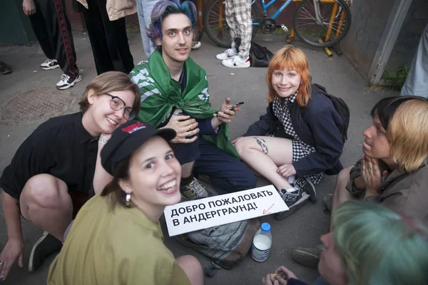 Una compañía de jóvenes vestidos a la moda se sienta alrededor de un cartel que dice "Bienvenido al metro ." — Foto de Stock