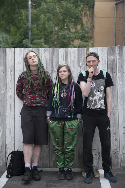 Deux jeunes hommes et une fille avec dreadlocks posent sur le fond d'une clôture en bois . — Photo