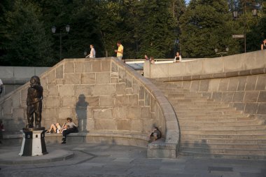 Güneşli bir yaz gününde Kırım köprüsüne bakan Gorky Park'taki setin merdivenlerinde oturan insanlar