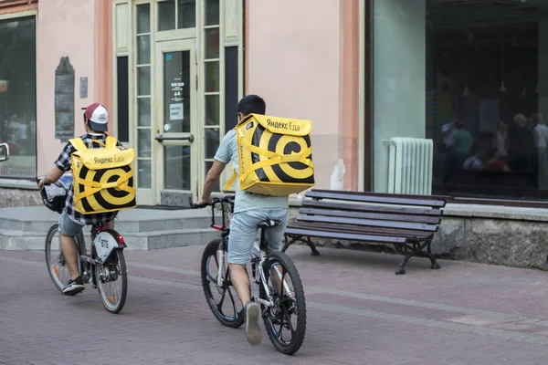 Доставка еды в Москву - курьер в шляпе с ушами и желтой курткой с надписью "Яндекс" еда и желтый рюкзак едет на велосипеде по улице — стоковое фото