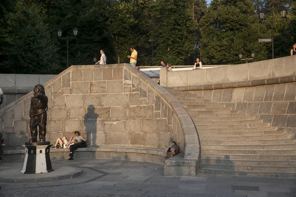 Mensen zitten op de trappen van de dijk in Gorky Park op een zonnige zomerdag met uitzicht op de Krim brug — Stockfoto