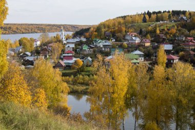 Rusya, Plyos - Ekim 04, 2019: Ivanovo Bölgesi. Volga nehrinin arka planında parlak sarı sonbahar ormanı. Katedral Dağı 'nın yüksekliğinden. Sonbahar güneşli bir günde Varvara kilisesi ve renkli evler.