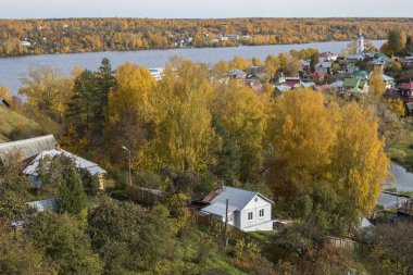 Rusya, Plyos - Ekim 04, 2019: Ivanovo Bölgesi. Volga nehrinin arka planında parlak sarı sonbahar ormanı. Katedral Dağı 'nın yüksekliğinden. Sonbahar güneşli bir günde Varvara kilisesi ve renkli evler.