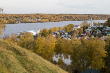 Rusya, Plyos - Ekim 04, 2019: Ivanovo Bölgesi. Volga nehrinin arka planında parlak sarı sonbahar ormanı. Katedral Dağı 'nın yüksekliğinden. Sonbahar güneşli bir günde Varvara kilisesi ve renkli evler.