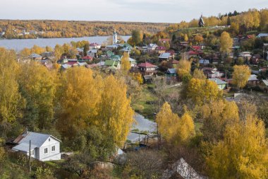 Rusya, Plyos - Ekim 04, 2019: Ivanovo Bölgesi. Volga nehrinin arka planında parlak sarı sonbahar ormanı. Katedral Dağı 'nın yüksekliğinden. Sonbahar güneşli bir günde Varvara kilisesi ve renkli evler.