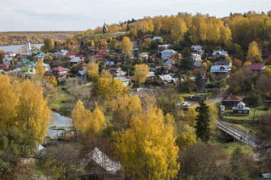 Rusya, Plyos - Ekim 04, 2019: Ivanovo Bölgesi. Volga nehrinin arka planında parlak sarı sonbahar ormanı. Katedral Dağı 'nın yüksekliğinden. Sonbahar güneşli bir günde Varvara kilisesi ve renkli evler.