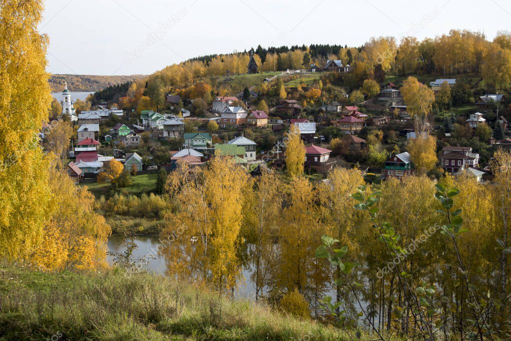 RUSSIA, Plyos - October 04, 2019: Ivanovo Region. Bright yellow autumn forest on background of Volga river. from height of Cathedral Mountain. Varvara church and colorful houses in autumn sunny day.