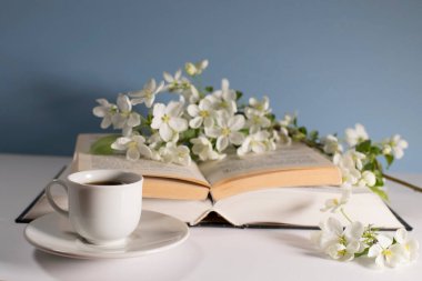 Çiçek açan bir elma ağacının dalı ya da açık bir kitap üzerinde kiraz ağacı ve mavi bir duvarın arka planında bir fincan kahve. Kavram - çevrimiçi öğrenme. Uzayı kopyala Eğitim çevrimiçi