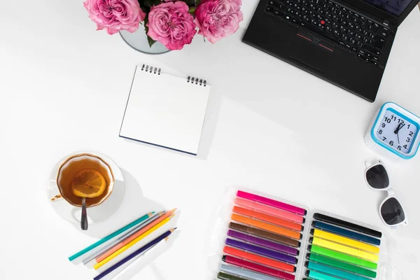 Laptop, notebook, felt-tip pens, watches, sunglasses, a cup of tea with lemon, pencils and a bouquet of red roses on the office desk. Frame.Copy space