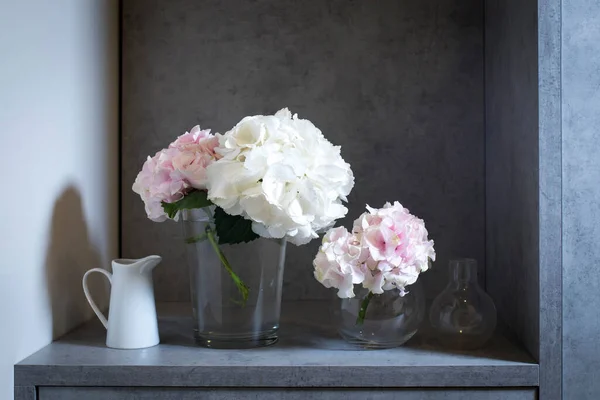 ガラスの花瓶にピンクと白のアジサイと灰色の工芸品の背景に白い磁器のジャグ — ストック写真