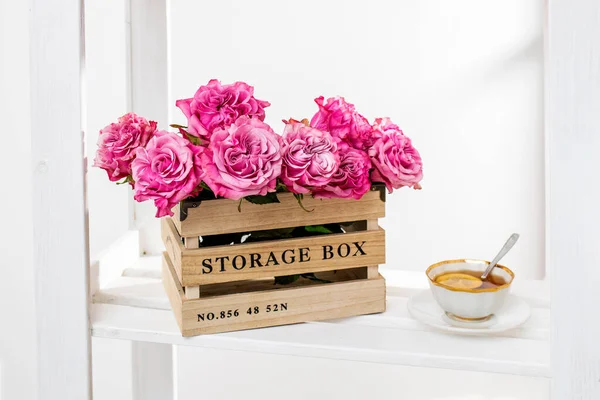 Wooden storage box with a bouquet of pink roses and cup of tea with lemon. Home decoration. Copy space