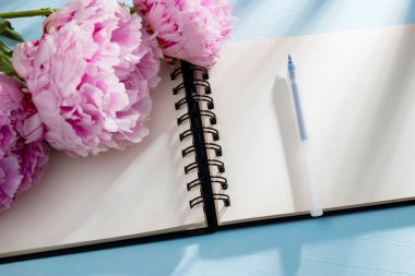 Üç taze çiçek açan pembe şakayık beyaz bir defterin üzerinde yatıyor. Mesaj için yer var. Liste yapmak için. Eğitici kavram